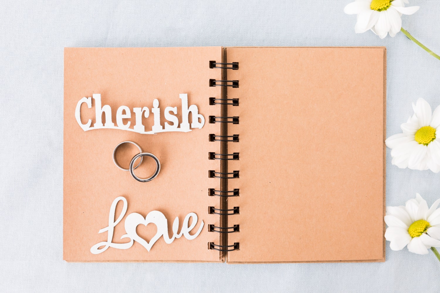 Craft paper notebook with 'Cherish' and 'Love' inscriptions and wedding rings, with daisies on side