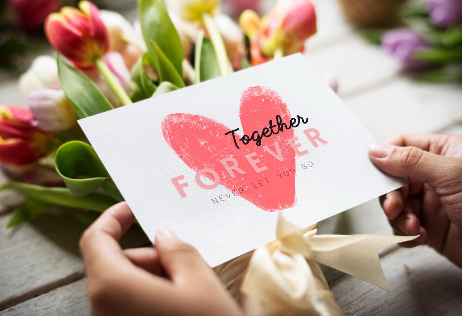 Valentine's Day greeting card with 'Together Forever' message, held over a bouquet of tulips.