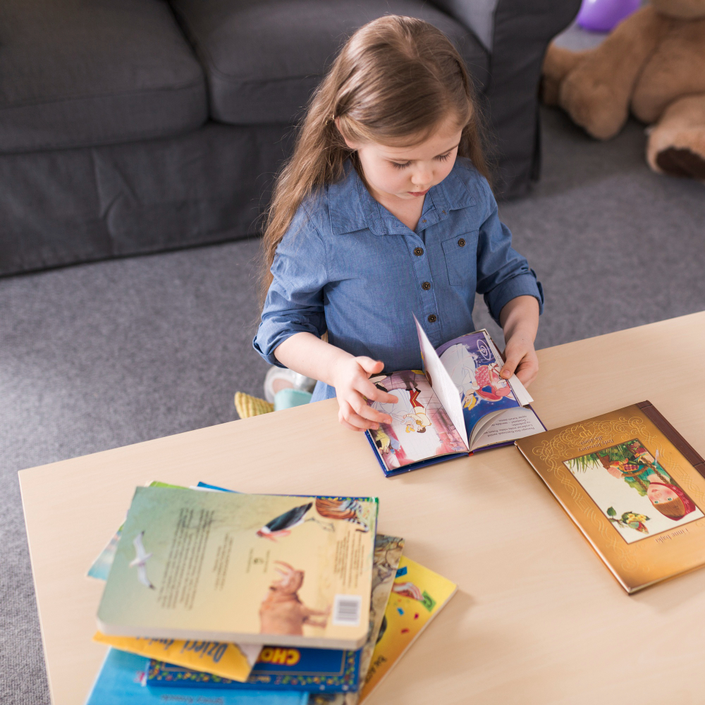 Adorable baby holding a colorful storybook, surrounded by other cute baby gifts and toys.